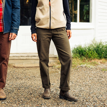 Two people wearing outdoor clothing standing on a gravel surface with a white building in the background.