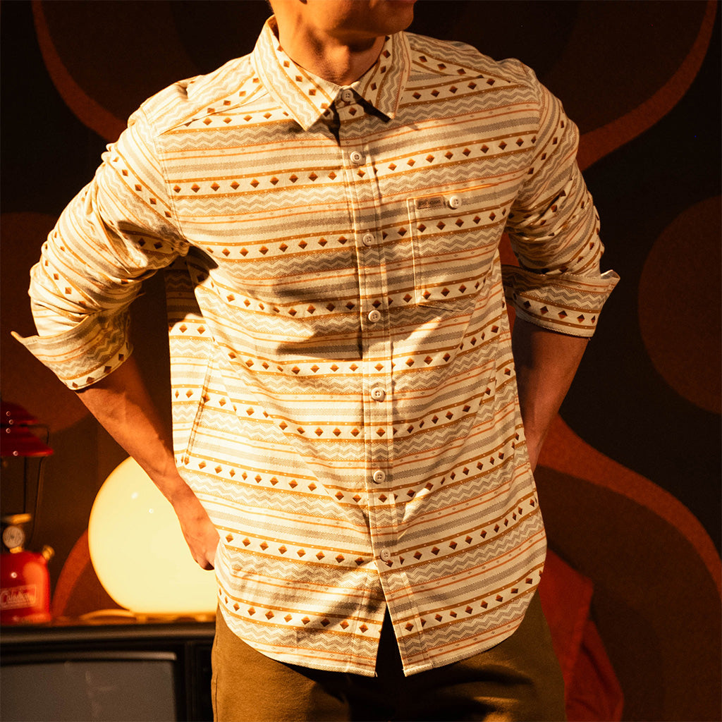 General lifestyle image of person wearing a "Bone White Sunset Stripe" Mountain Shirt Lightweight with a dark background with a warm glow in a dimly lit room.